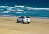Najpiękniejsze plaże Chorwacji na rodzinne wakacje samochodem – praktyczny przewodnik po sprawdzonych miejscach Biały SUV jedzie po piaszczystej plaży nad morzem w słoneczny dzień