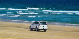 Najpiękniejsze plaże Chorwacji na rodzinne wakacje samochodem – praktyczny przewodnik po sprawdzonych miejscach Biały SUV jedzie po piaszczystej plaży nad morzem w słoneczny dzień