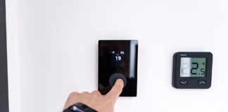 Automatyczne bilansowanie ciepła między kondygnacjami domu – czy smart głowice i czujniki rozwiążą problem przegrzewania Dłoń regulująca cyfrowy termostat w nowoczesnym wnętrzu domu