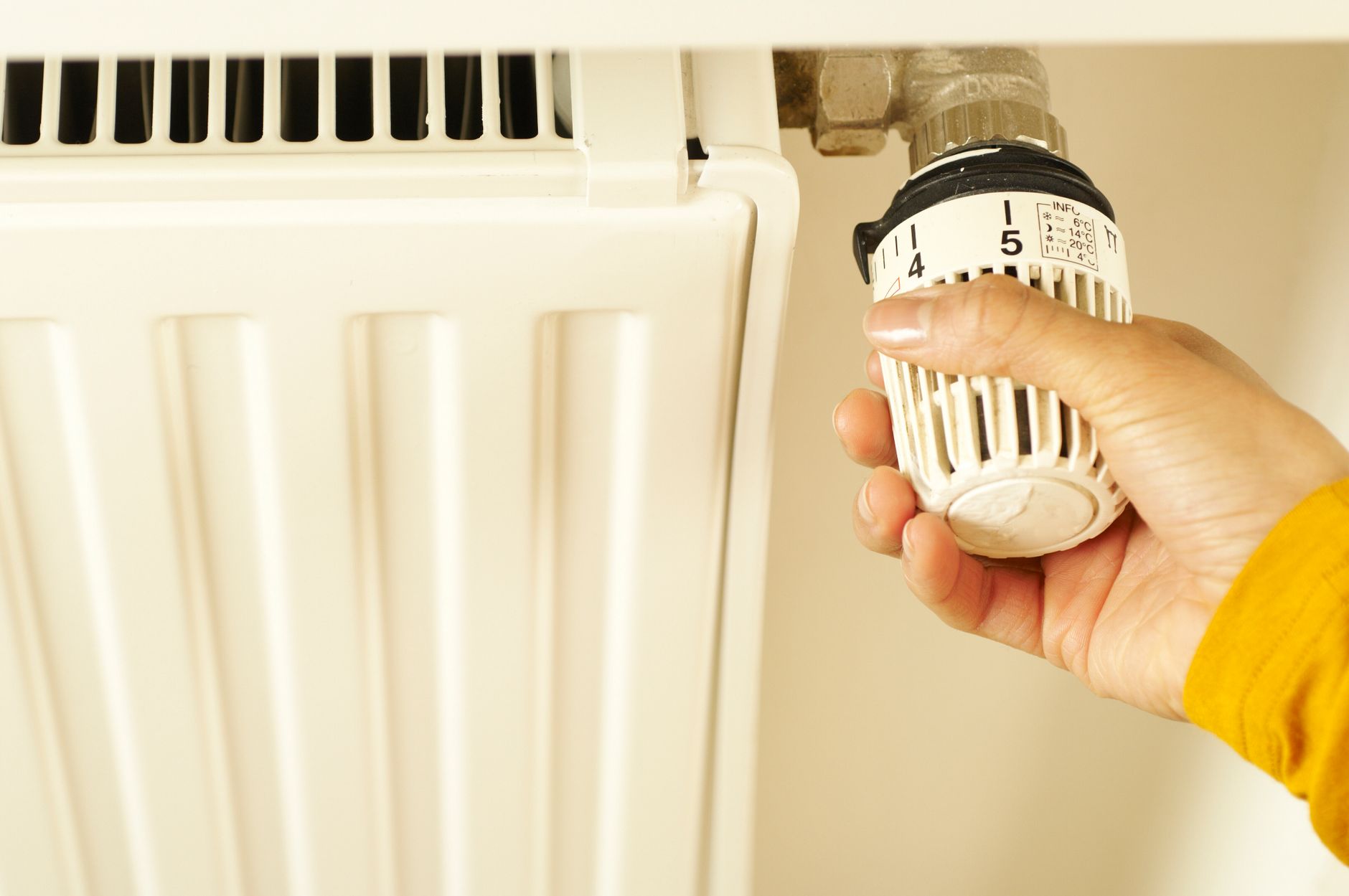 Dłoń reguluje termostat na grzejniku, ustawianie temperatury w domu